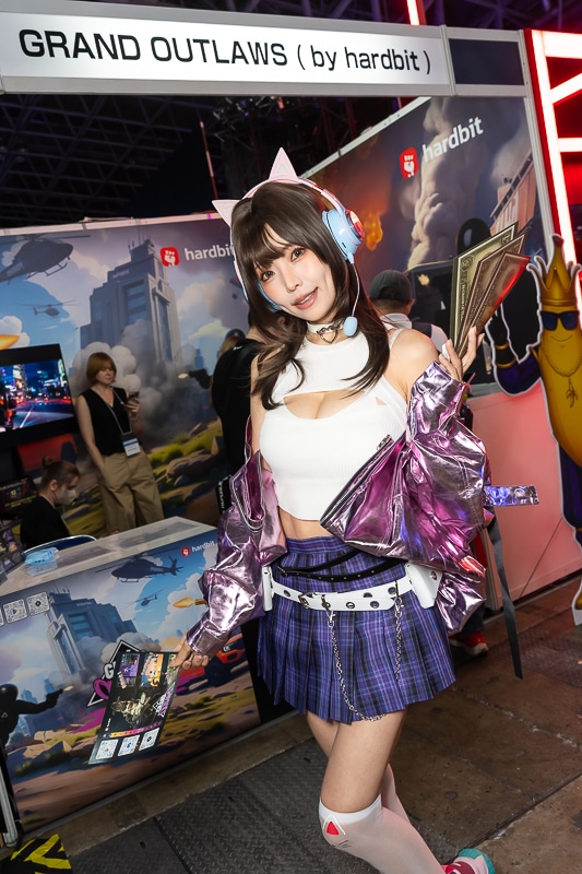 「東京ゲームショウ2025」の美人コスプレイヤー＆コンパニオン特集｜胸開きニット衣装がセクシーなコンパニオンが『Grand Outlaws』を大展開する「GRAND OUTLAWS」ブースでお出迎え